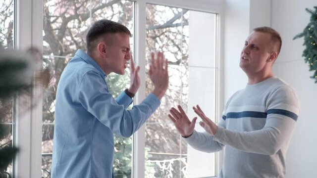 Male same sex couple swearing at home. Men friends swear and shout at each other