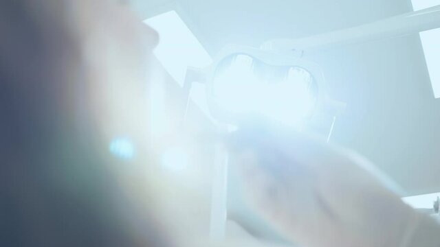 Low angle of a male dentist adjusting dental lamp to see better, while examining teeth of a female patient.
