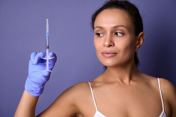 Natural beauty woman holding a syringe with rejuvenating injection in her hand, isolated on purple...