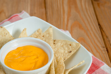 Cheddar on a bowl of nachos on a wooden table. The background is grey and there is a black and white kitchen cloth under the dish. Horizontal image