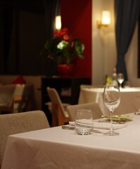 Empty wineglass and drinking glass with stainless steel tabelware on tablecloth with white napkin at night