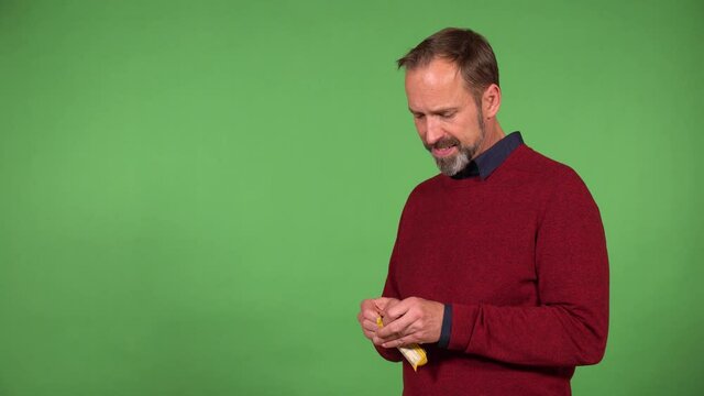 A middle-aged handsome Caucasian man eats a chocolate bar - green screen background