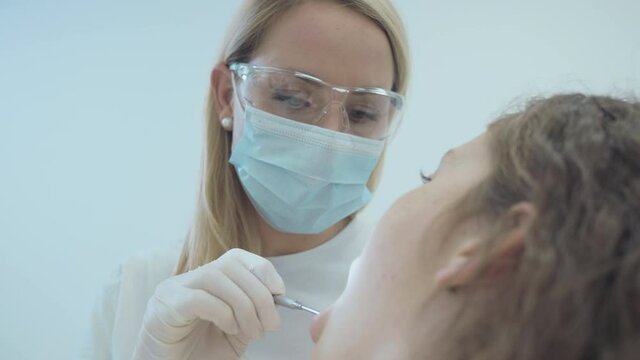 Low angle shot of Caucasian female dentist doing exam and checking up on oral health, teeth and gums of her female patient.