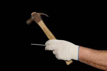 A hammer and a nail are held in a gloved hand. Isolate on black.