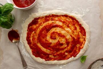 Pizza coooking process with sourdough homemade natural east dough, top view, tomatoes sauce and basil