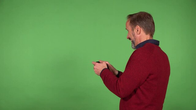A middle-aged handsome Caucasian man plays a game on the green screen background and holds a controller