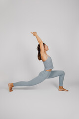Young woman posing. Brunette in fitness suit does yoga exercise, stands in warrior pose on isolated...