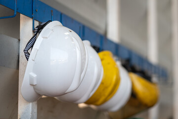Yellow and white safety helmet which is keep at metal rail rack at the factory wall, Industrial PPE...