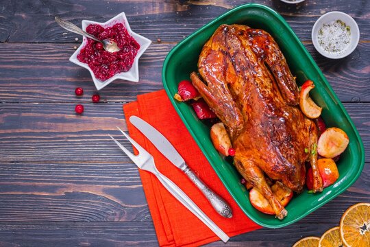 Whole baked duck with apples and cranberries in a green ceramic baking dish on a dark wooden background. Festive dishes for Christmas and New Year.