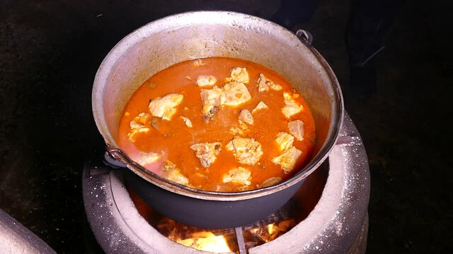 Goulash is prepared with seasoning and meat. Steam from a hot dish. Kitchen in a cauldron. Stir with a kitchen spatula. Campfire food.