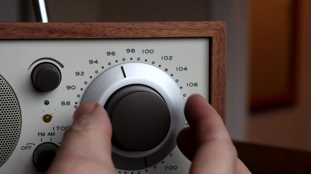 Hand turning circular tuner dial on old fashioned radio with wood veneers