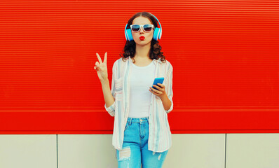 Portrait of young woman in headphones listening to music with smartphone on red background