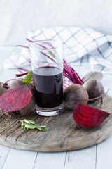 Tall glass of beet juice surrounded by whole and cut beets, on a rustic board.
