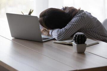 Exhausted tired office worker, employee woman sleeping at workplace, placing head on desk at...