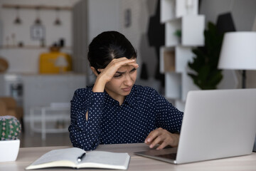 Tired upset Indian business woman working at laptop computer, looking at screen. Overworked...
