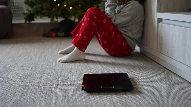 Electronic scale and in the background a young woman sitting on the floor frustrated and sad because of being overweight after the abundant meals on Christmas holidays.