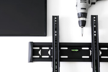 Black TV wall bracket, electric drill and monitor on a white background. The concept of mounting a TV or computer monitor on a wall. Bubble level - obrazy, fototapety, plakaty