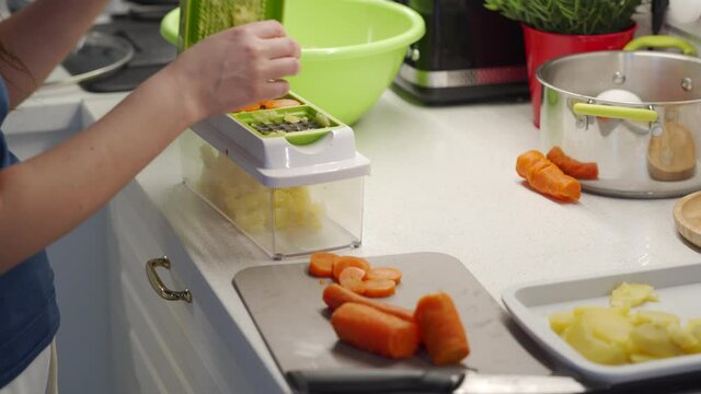 Woman cooking salad in the kitchen using a vegetable chopper with container, chop and slice boiled potatoes and carrot with food slicer on kitchen countertop closeup. High quality 4k footage
