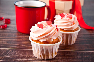 Valentines cupcakes cream cheese frosting decorated with heart candy, mug of coffee and gift box on the wooden background.