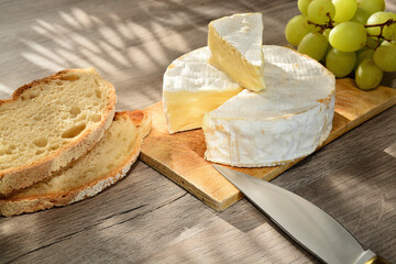 French camembert of Normandy served on wooden cutting board with grapes and slices of bread.