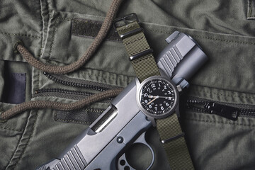 Vintage military watch and pistol on army jacket green background, Classic timepiece mechanical wristwatch, Military men fashion and accessories.