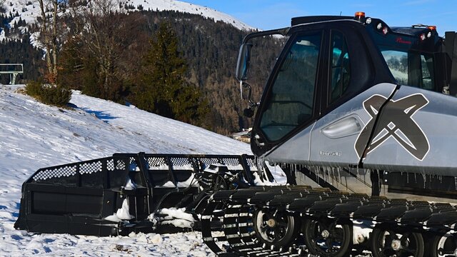 Front side of snow groomer vehicle Prinoth Leitwolf parked on ski slope of Donovaly ski resort Park Snow, some icicles visible on bottom of the cabin and chassis. Winter season january 2022