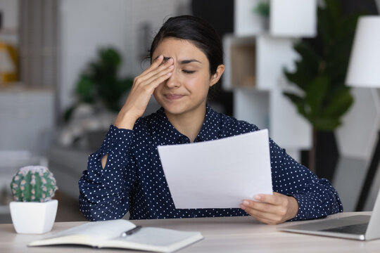 Stressed upset Indian employee holding document with bad dismissal news. Frustrated student girl receiving paper letter, rejection notice from business college, from college, feeling sad, unhappy