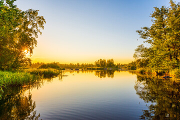 Fototapeta na wymiar Sunset over the river. Clear sky. Overgrown coastline. Smooth surface of water. Russia, Europe.
