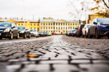 Fototapeta premium Autumn day in the city. The old pavement. The car is parked on the street. Focus on the stones. Close up view from the pavement level.