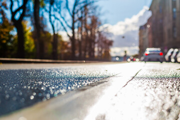 Sunny autumn day. The car drives off along the road. A row of parked cars on the street. The road after the rain. Focus on the asphalt. Close up view from the level of the dividing line.