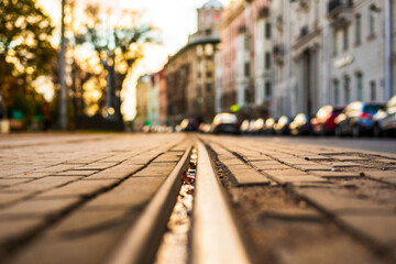 Sunny autumn day. A row of parked cars on the street. The old pavement. Sunset. Focus on the tram rail. Close up view of a tram rail level.