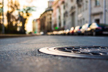 Sunny autumn day. A row of parked cars on the street. The road after the rain. Focus on the manhole cover. Close up view of a manhole cover at the level of the asphalt.