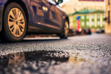 Rainy day in the city. A car drives by along the road. Rainy day in the city. The road after the rain. Focus on the asphalt. Close up view from the asphalt level.