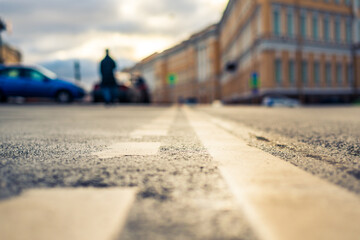 Rainy day in the city. A pedestrian is walking along the road. Historical center of the city. Focus on the asphalt. Close up view from the level of the dividing line.