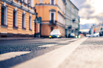 Rainy day in the city. Cars drive along the road. Car headlights. Historical center of the city. Focus on the asphalt. Close up view from the level of the dividing line.