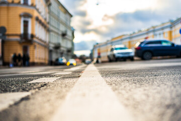 Cloudy autumn day in the city. Cars drive along the road. Car headlights. Historical center of the city. Focus on the asphalt. Close up view from the level of the dividing line.