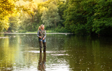 A woman stands in the river and fishes with a spinning rod