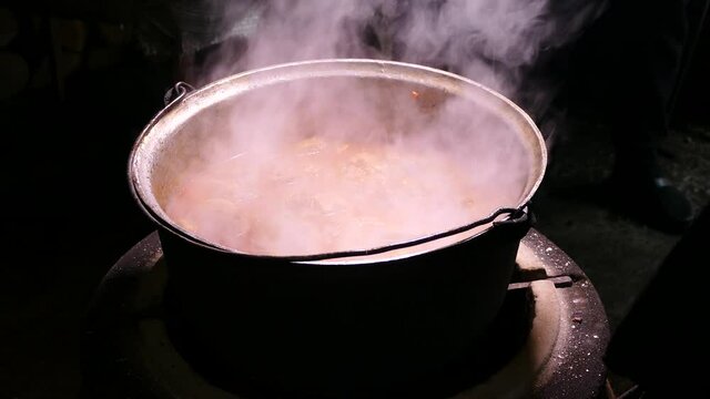 Goulash is prepared with seasoning and meat. Steam from a hot dish. Kitchen in a cauldron. Stir with a kitchen spatula. Campfire food.