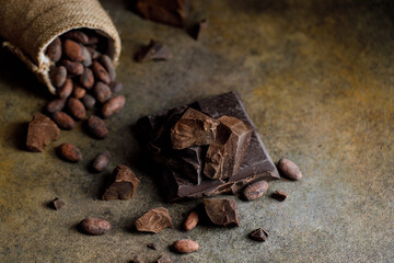 Pieces of dark chocolate with cocoa beans on brown background.	
