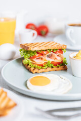Toast sandwich with gouda cheese and turkey ham filled with tomato and lettuce on a bright background with ingredients in blurry background. Served with coffee and orange juice and eggs