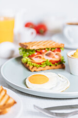 Toast sandwich with gouda cheese and turkey ham filled with tomato and lettuce on a bright background with ingredients in blurry background. Served with coffee and orange juice and eggs