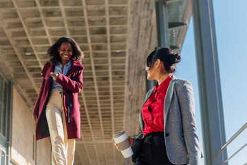 two multiethnic business women walking near an office building during a break from work.