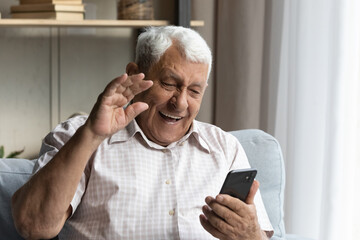 Happy elderly senior 80s retired man waving hand, looking at cellphone screen, starting web camera...