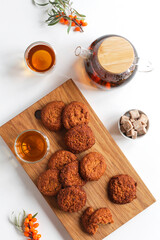 Vitamin tea with herbs and sea buckthorn, cereal gluten-free cookies with dried fruits on a wooden board. Healthy food, tea drinking.
White table, top view, copy space.