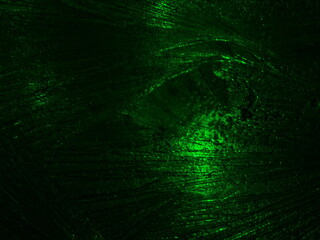 Frosty ice patterns on glass in green light.