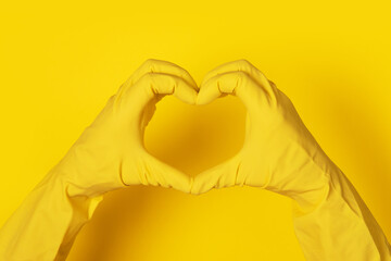 Fototapeta premium Hands in gloves making heart shape over yellow background, love cleanliness concept