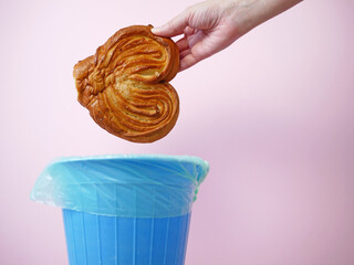 Hand throwing sweet bun away, trash bin, food waste, goodbye excess weight and sweets addiction concept, diet concept