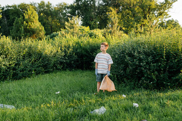 A seven-year-old boy at sunset is engaged in garbage collection in the park. Environmental care,...