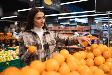 Young woman customer choosing fresh oranges on the supermarket