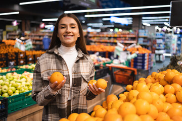 Portrait of smiling woman who holding oranges in fruit and vegetable section of supermarket
